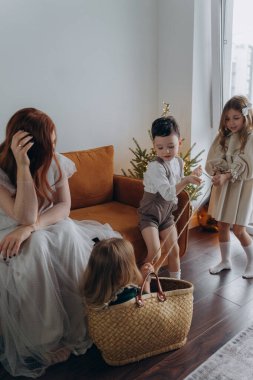 Kızları ve oğluyla birlikte beyaz bohem elbiseler giymiş güzel bir kızıl kadın Noel arifesinde birlikte vakit geçiriyorlar ve en küçük kız sepette oturuyor.