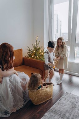 Kızları ve oğluyla birlikte beyaz bohem elbiseler giymiş güzel bir kızıl kadın Noel arifesinde birlikte vakit geçiriyorlar ve en küçük kız sepette oturuyor.