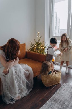 Kızları ve oğluyla birlikte beyaz bohem elbiseler giymiş güzel bir kızıl kadın Noel arifesinde birlikte vakit geçiriyorlar ve en küçük kız sepette oturuyor.