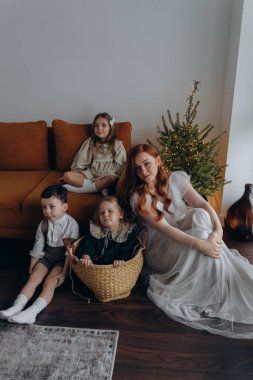 Kızları ve oğluyla birlikte beyaz bohem elbiseler giymiş güzel bir kızıl kadın Noel arifesinde birlikte vakit geçiriyorlar ve en küçük kız sepette oturuyor.