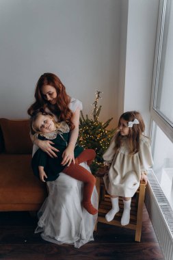 Beyaz bohem elbiseli güzel kızıl kadın ve küçük kızları Noel arifesinde birlikte vakit geçiriyorlar.