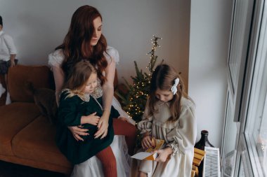 Beyaz bohem elbiseli güzel kızıl kadın ve küçük kızları Noel arifesinde birlikte vakit geçiriyorlar.