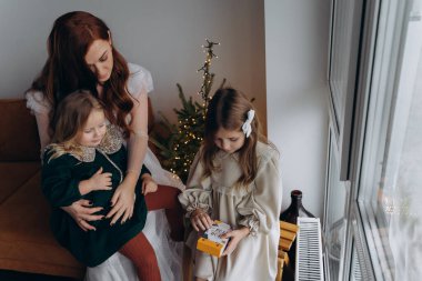 Beyaz bohem elbiseli güzel kızıl kadın ve küçük kızları Noel arifesinde birlikte vakit geçiriyorlar.