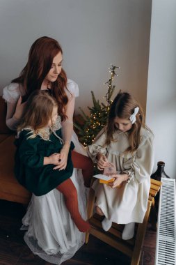 Beyaz bohem elbiseli güzel kızıl kadın ve küçük kızları Noel arifesinde birlikte vakit geçiriyorlar.