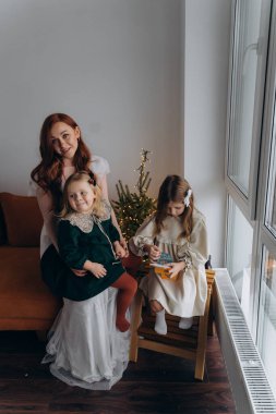 Beyaz bohem elbiseli güzel kızıl kadın ve küçük kızları Noel arifesinde birlikte vakit geçiriyorlar.