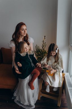 Beyaz bohem elbiseli güzel kızıl kadın ve küçük kızları Noel arifesinde birlikte vakit geçiriyorlar.