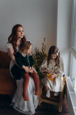 Beyaz bohem elbiseli güzel kızıl kadın ve küçük kızları Noel arifesinde birlikte vakit geçiriyorlar.