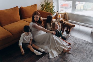 Oğlu ve küçük tatlı kızlarıyla birlikte beyaz bohem elbiseler giymiş güzel kızıl saçlı kadın kanepedeki evlerinde köpekleriyle vakit geçiriyorlar.