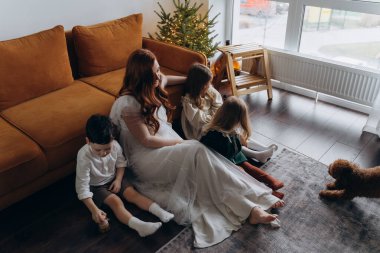 Oğlu ve küçük tatlı kızlarıyla birlikte beyaz bohem elbiseler giymiş güzel kızıl saçlı kadın kanepedeki evlerinde köpekleriyle vakit geçiriyorlar.