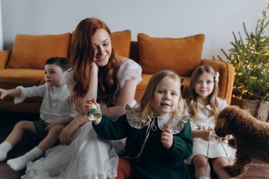 Oğlu ve küçük tatlı kızlarıyla birlikte beyaz bohem elbiseler giymiş güzel kızıl saçlı kadın kanepedeki evlerinde köpekleriyle vakit geçiriyorlar.