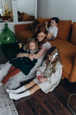 Oğlu ve tatlı küçük kızlarıyla birlikte beyaz bohem elbiseler giymiş güzel kızıl saçlı kadın kanepede birlikte vakit geçiriyorlar.