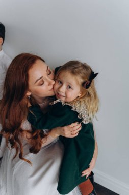 Beyaz bohem elbiseli güzel kızıl saçlı kadın küçük kızıyla temas kuruyor. Odada beyaz bir duvarın önünde. 