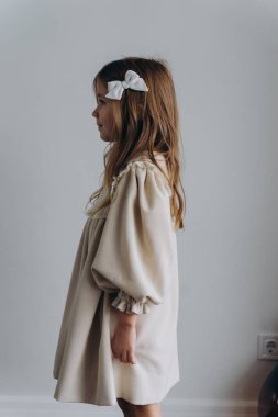 Güzel bir bohem elbisesi giymiş, duvarın yanındaki ahşap zeminde poz veren tatlı küçük bir kız, profilde duran bir kız.