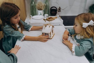 Çocuklar mutfaktaki masada zencefilli kurabiye evini inceliyor. 