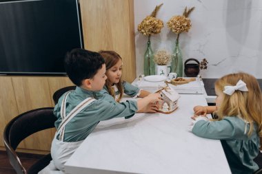 Çocuklar mutfaktaki masada zencefilli kurabiye evini inceliyor. 