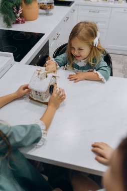 Çocuklar mutfaktaki masada zencefilli kurabiye evini inceliyor. 