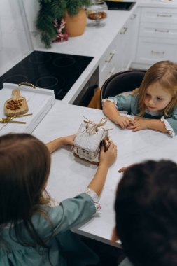 Çocuklar mutfaktaki masada zencefilli kurabiye evini inceliyor. 
