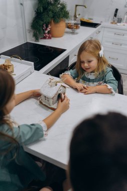 Çocuklar mutfaktaki masada zencefilli kurabiye evini inceliyor. 