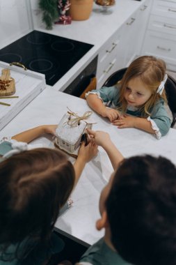 Çocuklar mutfaktaki masada zencefilli kurabiye evini inceliyor. 