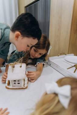 Çocuklar mutfaktaki masada zencefilli kurabiye evini inceliyor. 