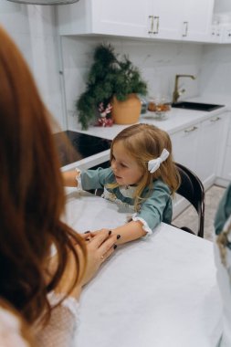 Beyaz bohem elbiseli güzel kızıl saçlı kadın ve küçük kızları mutfakta zencefilli kurabiye yiyorlar.  