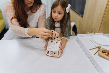 Beyaz bohem bir elbise giymiş güzel kızıl saçlı kadın ve küçük kızları mutfakta zencefilli kurabiye evlerinin paketlerini açıyorlar.  