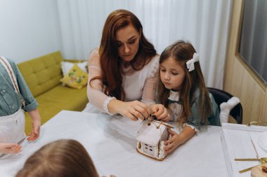Kızları ve oğluyla birlikte beyaz bohem bir elbise giymiş güzel kızıl saçlı kadın mutfakta zencefilli kurabiye paketlerini açıyor.  
