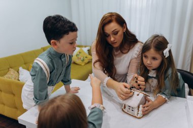 Kızları ve oğluyla birlikte beyaz bohem bir elbise giymiş güzel kızıl saçlı kadın mutfakta zencefilli kurabiye paketlerini açıyor. 