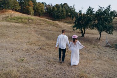 Kırsal kesimde güzel bir çift, arkadan bakınca beyaz elbiseli yakışıklı sakallı adam ve kadın el ele yürüyorlar.