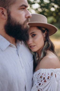 Kırsalda güzel bir çift, yakışıklı sakallı adam beyaz elbiseli kadına sarılıyor. 