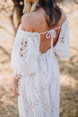 Arkadan görünüşlü güzel bir kadın. Renkli saçları ve dövmeli bir vücudu var. Kırsalda beyaz, uzun, boho tarzı bir elbise giymiş. 