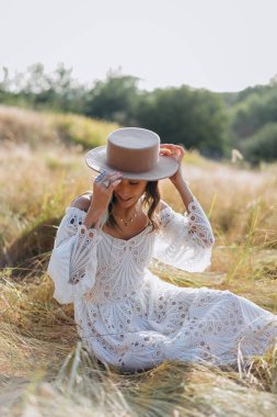 Güzel bir kadın. Renkli saçları ve dövmeli bir vücudu var. Beyaz, uzun bir boho tarzı elbise ve şapkası var.