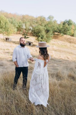 Kırsalda güzel bir çift, beyaz elbiseli bir kadının elini tutan yakışıklı sakallı bir adam. 