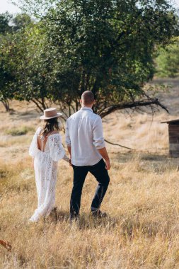 Kırsalda güzel bir çift, beyaz elbiseli yakışıklı sakallı adam ve kadın el ele tutuşuyorlar.