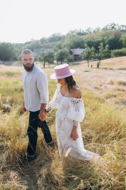Kırsalda güzel bir çift, beyaz elbiseli yakışıklı sakallı adam ve kadın el ele tutuşuyorlar.