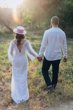 Kırsal kesimde güzel bir çift, arkadan görünüşlü beyaz elbiseli yakışıklı adam ve kadın el ele tutuşuyorlar.