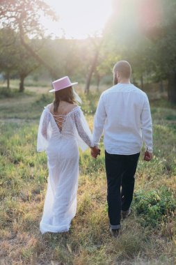 Kırsalda güzel bir çift, beyaz elbiseli yakışıklı sakallı adam ve kadın el ele tutuşuyorlar.
