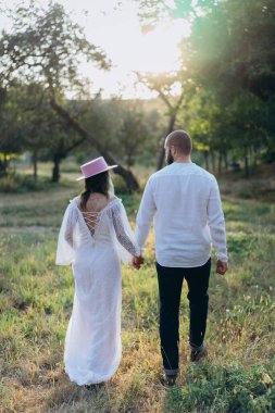 Kırsalda güzel bir çift, beyaz elbiseli yakışıklı sakallı adam ve kadın el ele tutuşuyorlar.