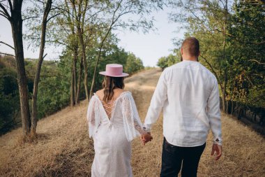 Kırsal kesimde güzel bir çift, arkadan görünüşlü beyaz elbiseli yakışıklı adam ve kadın el ele tutuşuyorlar.