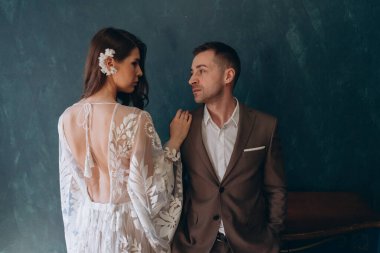 Beyaz bir bohem elbisesi içinde genç ve güzel gelin yarım dönüş yapıp mavi odada zarif bir takım elbise giymiş damadına dönüyor.