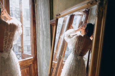 Kızın güzel beyaz bohem tüllü elbisesinin aynadaki yansıması balkonun kapısını açıyor ve sırtı kameraya dönük.