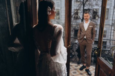 Zarif takım elbiseli bir adam balkonda sevgilisinin önünde duruyor ve balkonun kapısında duran güzel, beyaz, şehvetli bir tül elbise giymiş bir kız. 