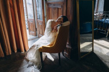  Balkonun yanındaki sandalyede oturan ve kameraya bakan güzel, beyaz, bohem tül elbiseli kız.