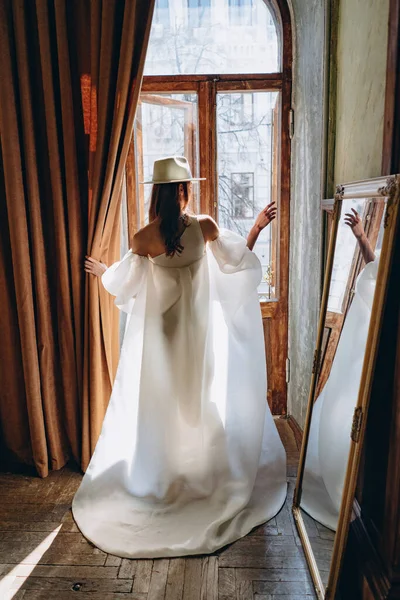 美しい白い官能的なドレスを着た女の子とカメラに戻る彼女とバルコニーへの入り口に立つ白い帽子 — ストック写真