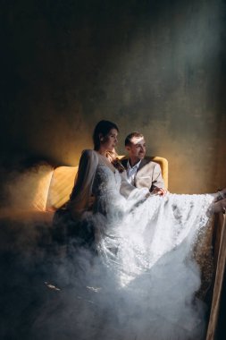 Zarif takım elbiseli bir adam sandalyede oturuyor. Yanında da güzel, beyaz tenli, tüllü bir kız var.