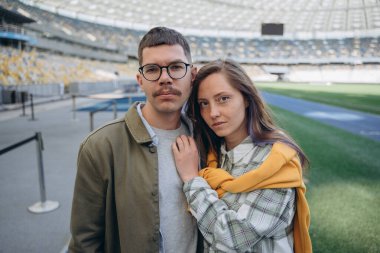 Boş bir stadyumda ayakta durup kucaklaşan bir çiftin fotoğrafı.