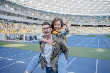 Boş stadyumda oynaşan bir çiftin fotoğrafı, kız arkadaşını sırtında taşıyan adam.