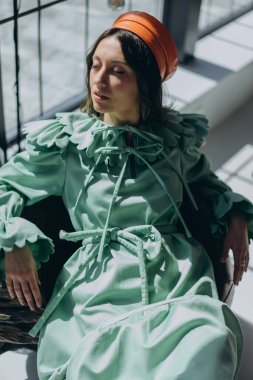 Tasarımcı yeşil elbiseli, parlak yakalı ve stüdyoda poz veren göz kamaştırıcı bir kadının moda fotoğrafı.