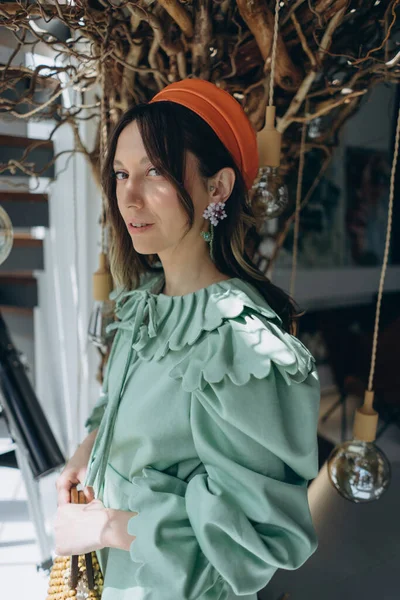 明るい襟と赤い帽子を持つデザイナーの緑のドレスを着た魅力的な女性のファッション写真がスタジオでポーズをとっています — ストック写真