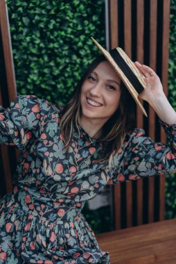 Stüdyoda şık bir çiçekli elbise ve hasır şapka giymiş güzel bir kadının fotoğrafı.